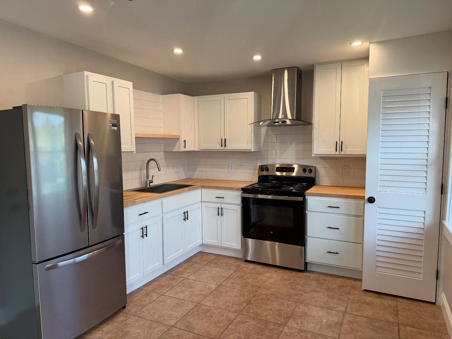 White shaker kitchen with butcher-block countertops and subway tile backsplash by I&I Home Repair