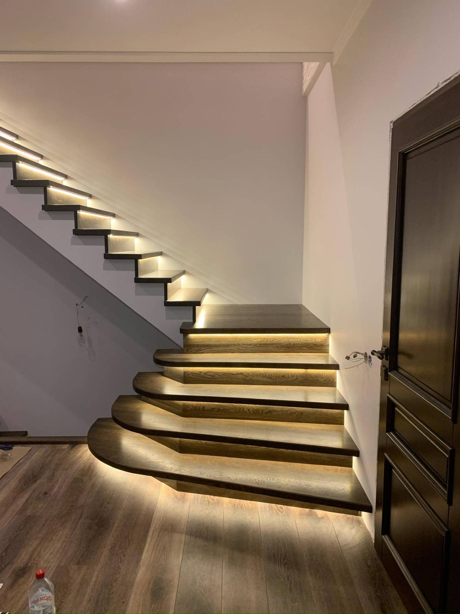 Dark wood staircase with curved lower steps by I&I Home Repair